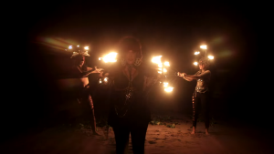 Screenshot from Metamorph's new video for Hex, showing witches dancing on a beach with fire.