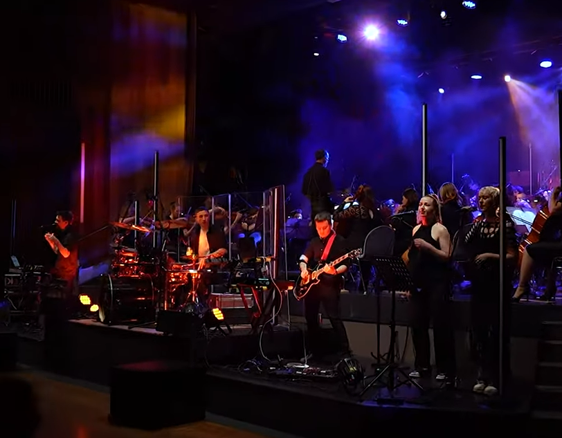 Screenshot of Slovenian electronic rock band playing with the Glasbena Šola Symphonic Orchestra of Krško. .